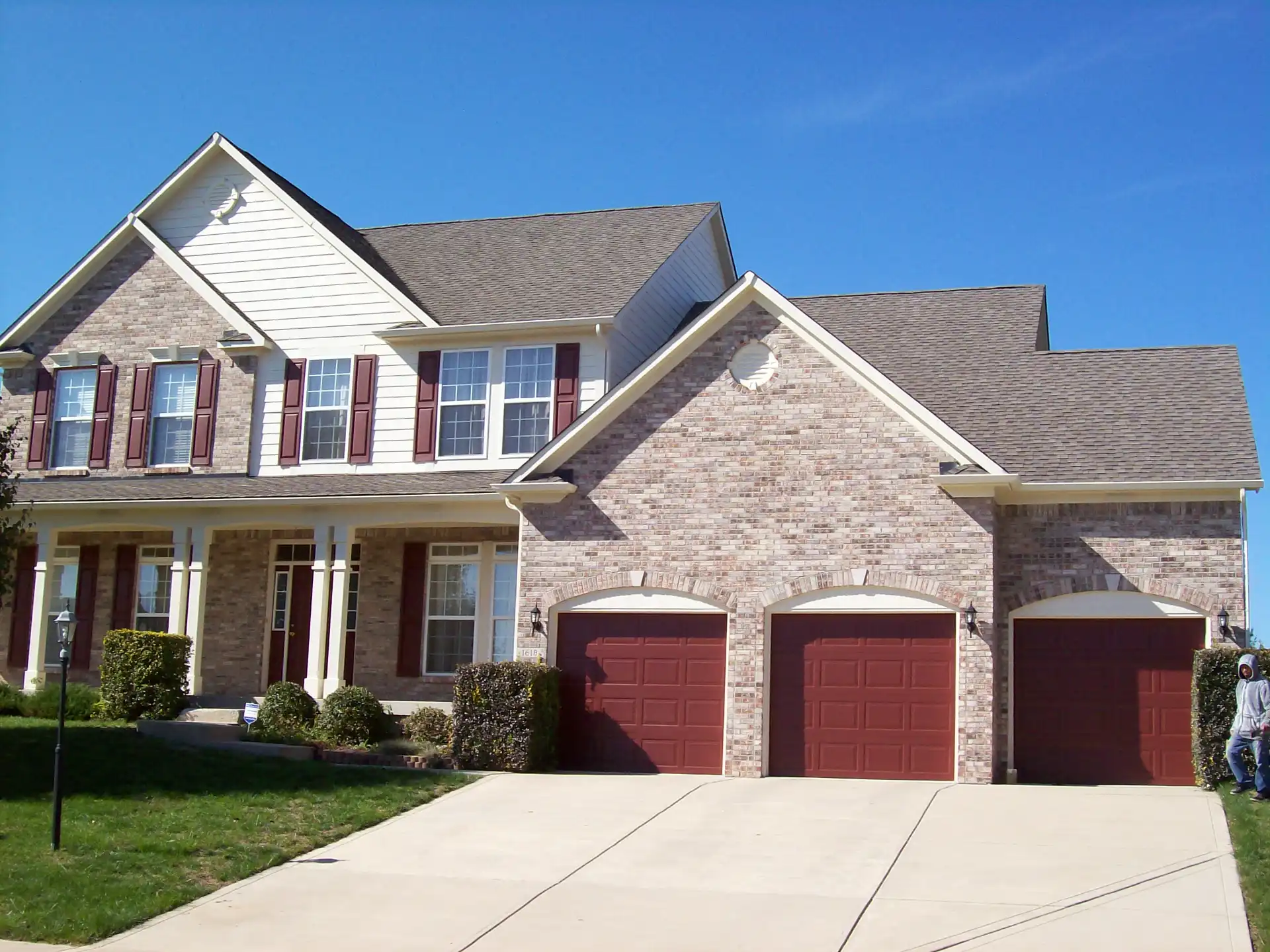 Central Indiana home exterior after Guy Painting's cream siding repaint with burgundy shutters and garage doors