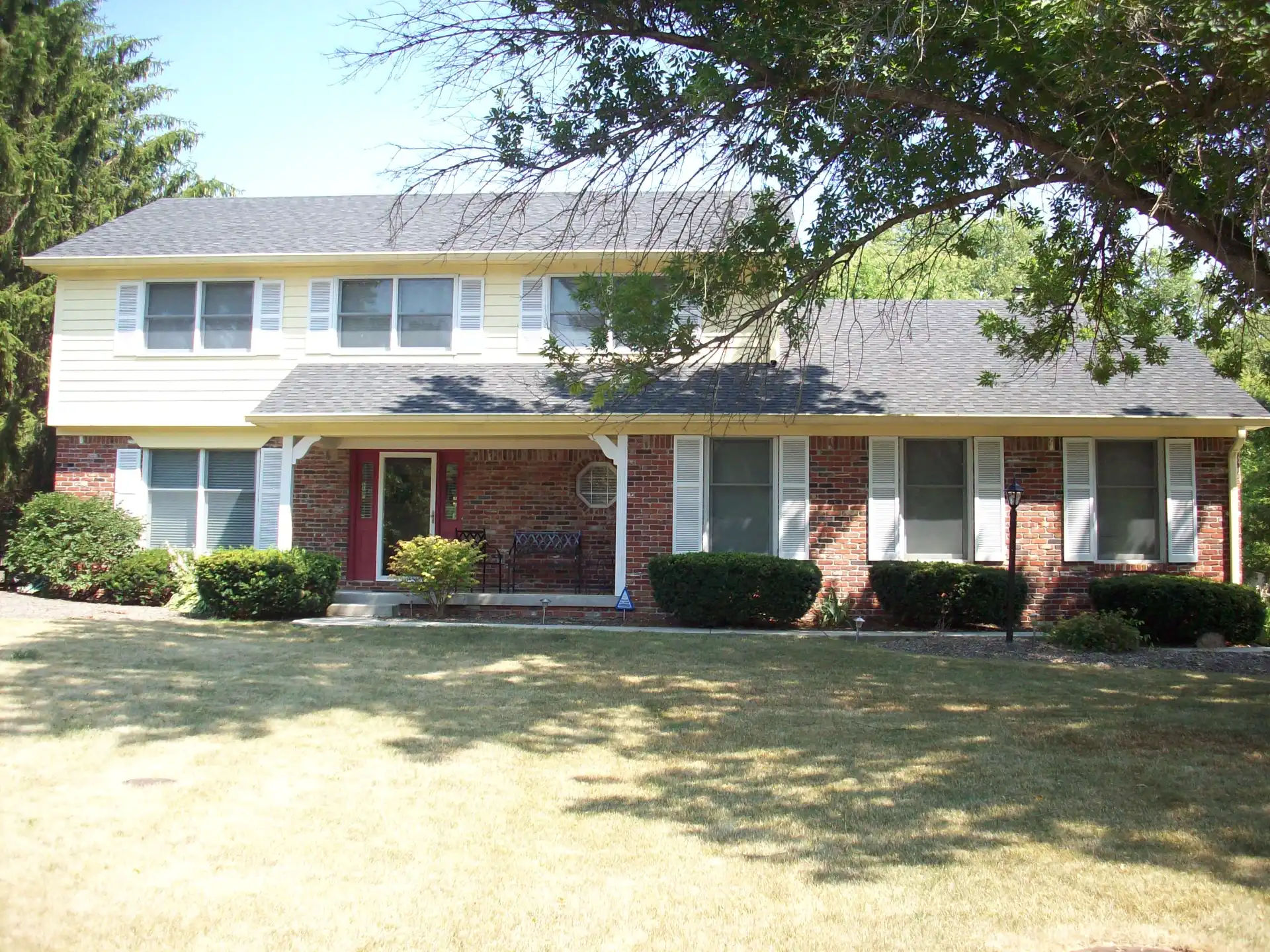 Central Indiana two-story home exterior after Guy Painting's warm cream siding repaint with white shutters and a red front door