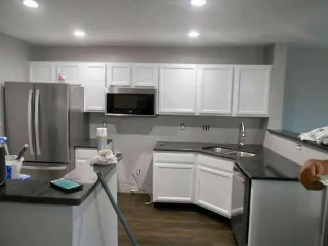 A completed kitchen renovation in Geist showcasing the clean and bright results of painting kitchen cabinets antique white by guy painting. The image features a full set of shaker-style upper and lower cabinets finished in a smooth, professional antique white that contrasts sharply with the dark granite countertops. A stainless steel French door refrigerator and over-the-range microwave are integrated into the new layout, while the dark wood-look flooring anchors the space. This transformation by guy painting demonstrates how a professional paint application can modernize a kitchen while maintaining a classic, high-end aesthetic.